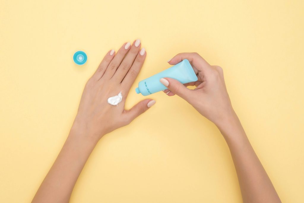 Woman applying sunscreen on hand with small blue tube on yellow background
